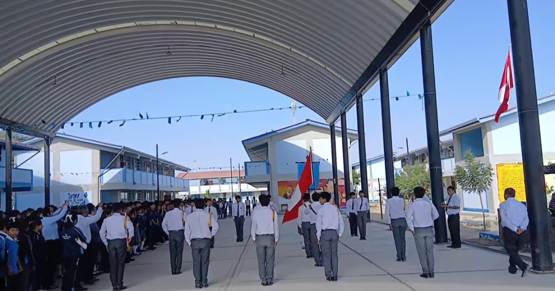 La imagen captura una ceremonia escolar en tablazo, únion, donde estudiantes uniformados se alinean para honrar la bandera peruana. La escolta de la bandera se prepara para un acto de patriotismo y respeto en la institución educativa.