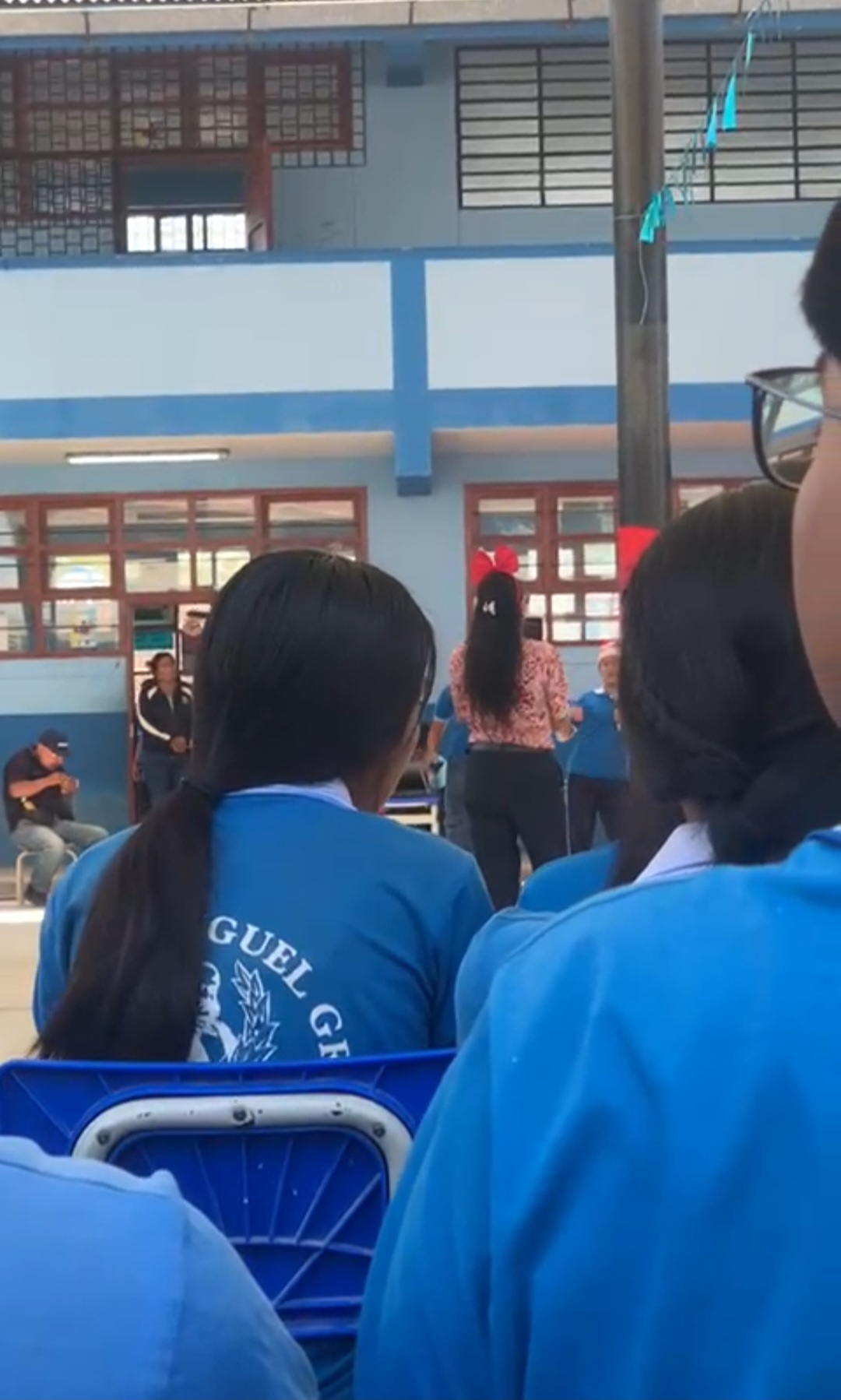 En la I.E. Almirante Miguel Grau, se desarrollan selecciones de cantos de villancicos. Los estudiantes en uniformes azules están sentados observando a los participantes en el escenario, en un ambiente festivo y navideño.